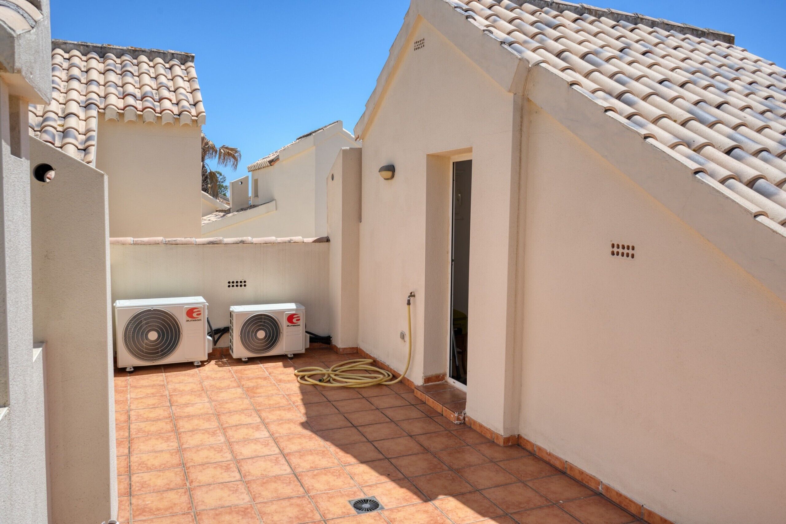 A narrow courtyard with two air conditioning units, a tiled floor, and a building with a tiled roof.