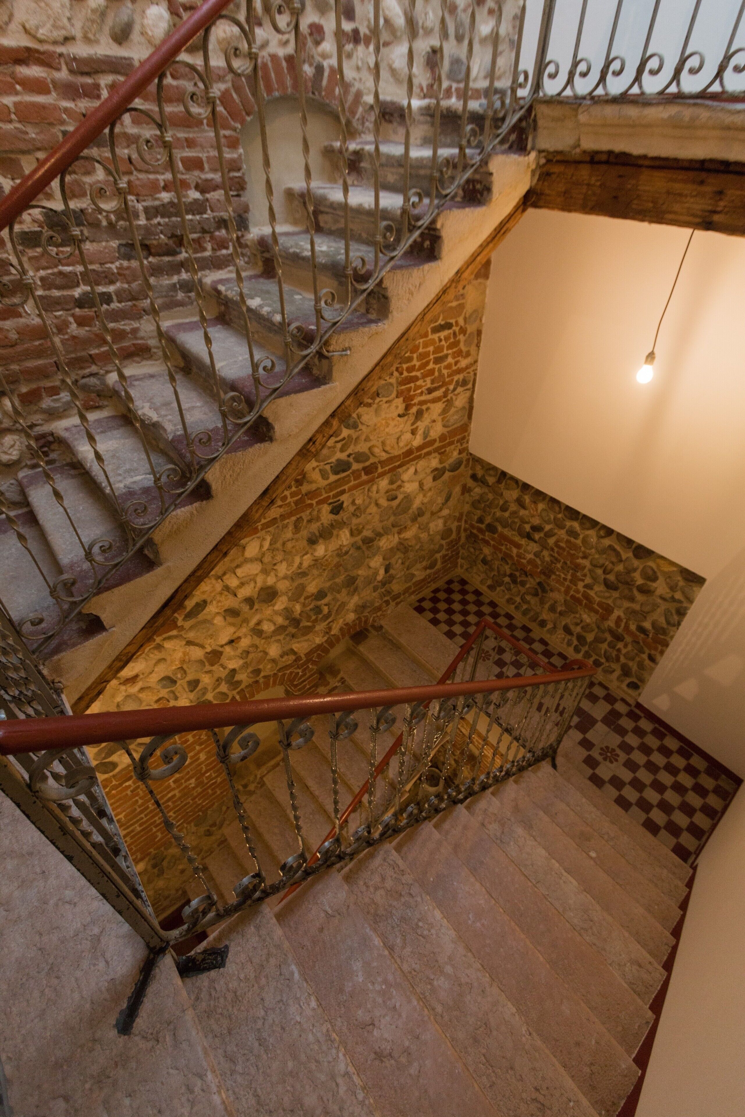 A staircase with ornate metal railings, stone walls, and a checkered floor pattern.