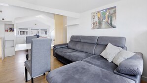 A modern living room with a grey sofa, a dining table, and a kitchen in the background. - Holiday Home 'Seaview Apartment Poreć Umgebung' with Sea View and Air Conditioning (Tar)