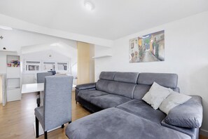 Una sala moderna con un sofá gris, una mesa de comedor y una cocina al fondo.