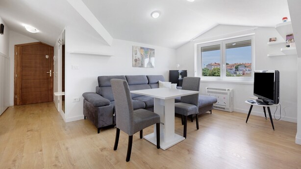 A modern living room with a grey sofa, a white dining table, and a TV on a stand. - Holiday Home 'Seaview Apartment Poreć Umgebung' with Sea View and Air Conditioning (Tar)