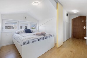 Un dormitorio con cama, ventana, puerta y suelo de madera.