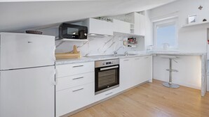 A modern kitchen with white cabinetry, a built-in oven, a microwave, and a bar stool. - Holiday Home 'Seaview Apartment Poreć Umgebung' with Sea View and Air Conditioning (Tar)