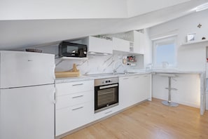 A modern kitchen with white cabinetry, a built-in oven, a microwave, and a bar stool.