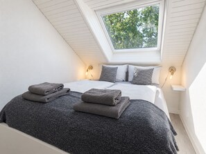 Ein Schlafzimmer mit Dachfenster, einem Bett mit grauer Strukturdecke, zwei Nachttischlampen und einem kleinen Nachttisch.