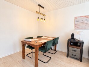 Ein Essbereich mit einem Holztisch, grün gepolsterten Stühlen, einer Deckenleuchte und einem kleinen Beistelltisch mit einer Lampe.