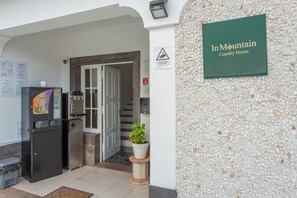 Een receptiegedeelte met een bord waarop 'In Mountain Country House' staat, een waterdispenser, een koelkast en een potplant.