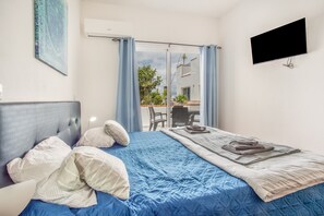 A bedroom with a bed, a flat-screen TV, and a view of an outdoor area. - Apartment 'Pool  View' with Shared Pool, Shared Garden and Wi-Fi (Gaula)