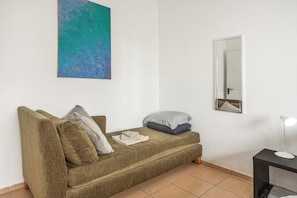 A room with a sofa, pillows, a small table with a lamp, a painting on the wall, and a mirror. - Apartment 'Pool  View' with Shared Pool, Shared Garden and Wi-Fi (Gaula)