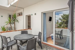 A patio area with a round table and chairs, a potted plant, and a sliding glass door leading to an outdoor space. - Apartment 'Pool  View' with Shared Pool, Shared Garden and Wi-Fi (Gaula)