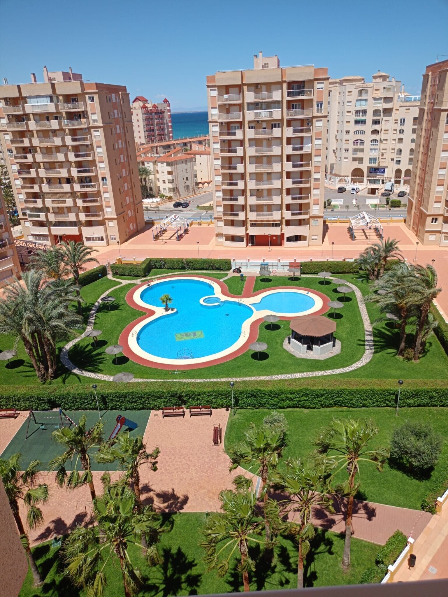 Un quartier résidentiel avec de grands immeubles, une piscine centrale et des espaces verts bien entretenus.