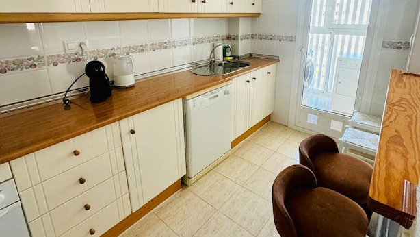 Una cocina con gabinetes blancos, una encimera de madera, una cafetera, un fregadero y una ventana con vistas.