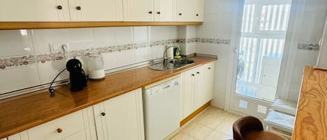 A kitchen with white cabinets, a wooden countertop, a coffee maker, a sink, and a window with a view.