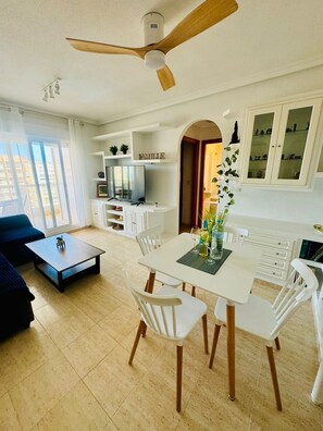Una sala de estar moderna con comedor, ventilador de techo, televisor y vista al exterior.