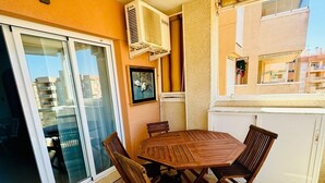 Un balcón con una mesa y sillas de madera, una puerta corrediza de vidrio y un equipo de aire acondicionado.