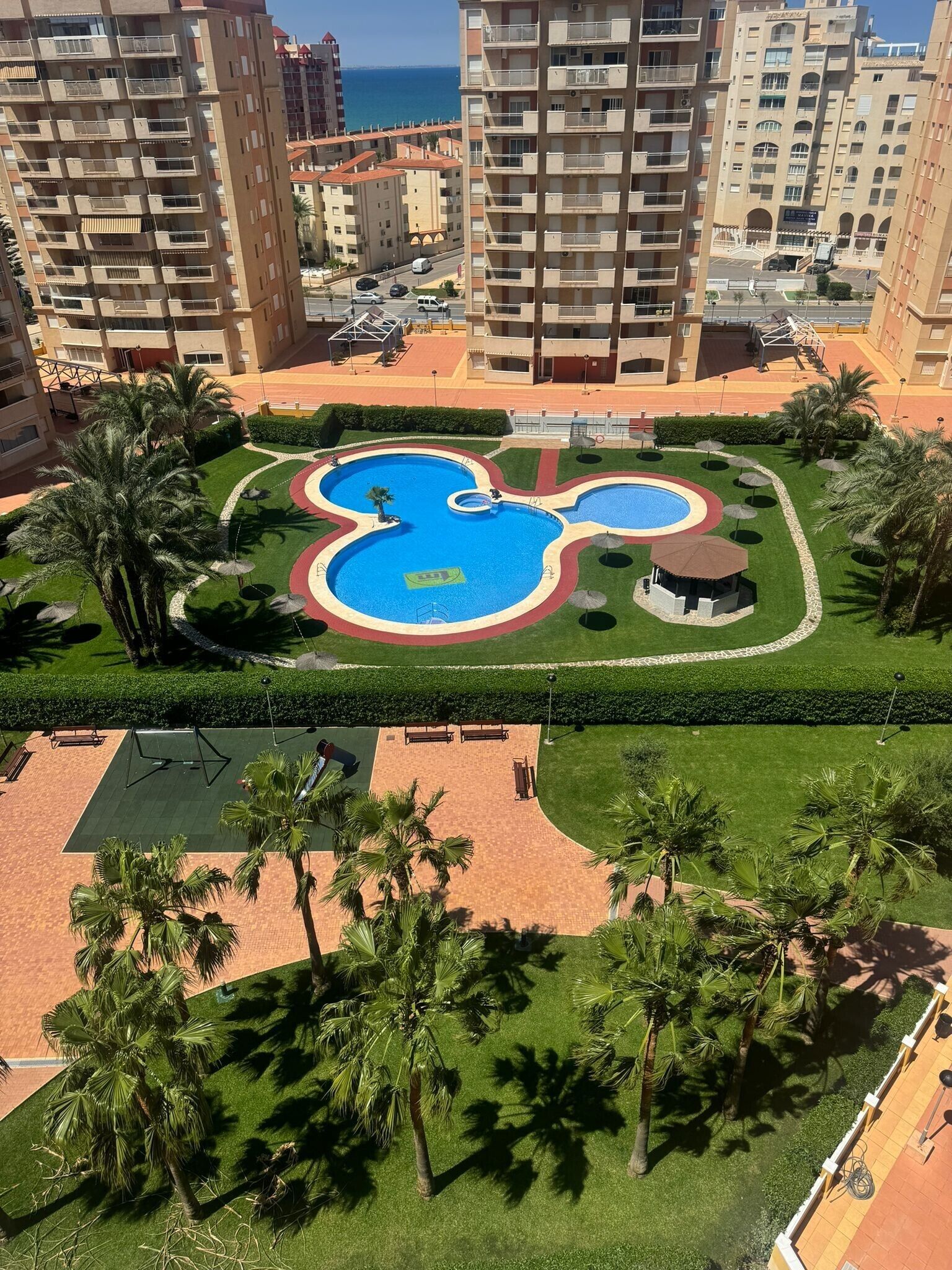 Ein Wohngebiet mit einem Mickey-Mouse-förmigen Schwimmbad, umgeben von Palmen und einem gepflegten Rasen.