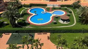 Ein Wohngebiet mit einem Mickey-Mouse-förmigen Schwimmbad, umgeben von Palmen und einem gepflegten Rasen.