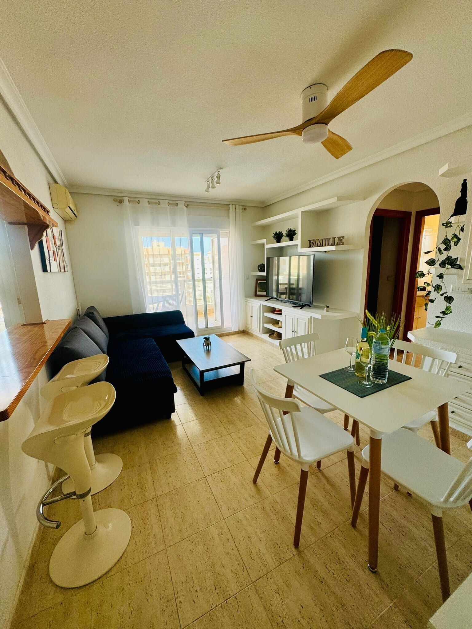 En moderne stue med sofa, spisebord, stole, en ventilator og et fjernsyn.
