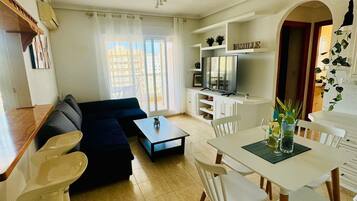En moderne stue med sofa, spisebord, stole, en ventilator og et fjernsyn.