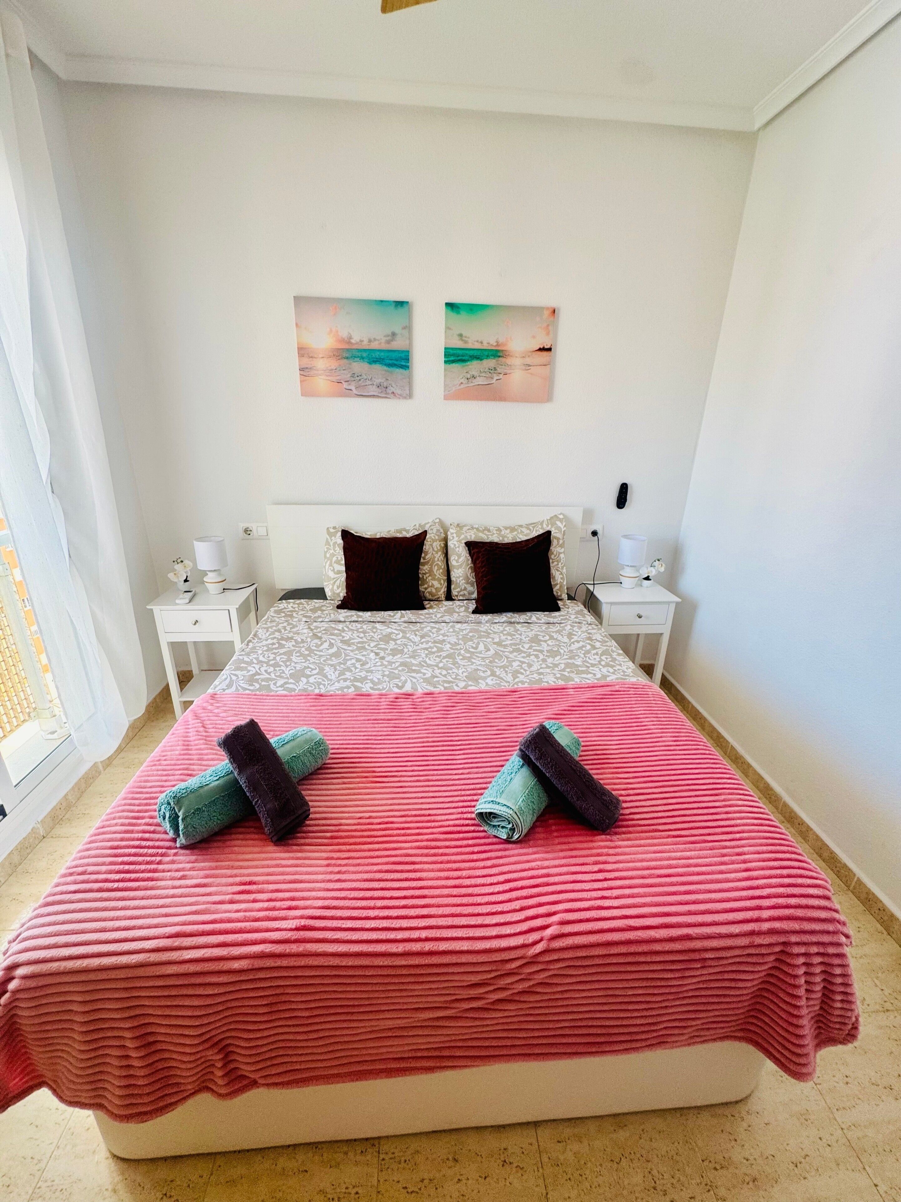 A bedroom with a bed, two nightstands, a window, and two wall art pieces.