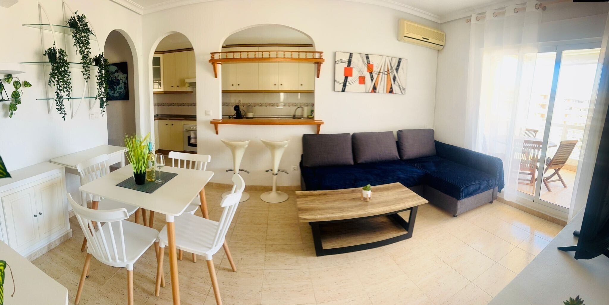 A modern living room with a sofa, dining table, chairs, and a kitchen in the background.