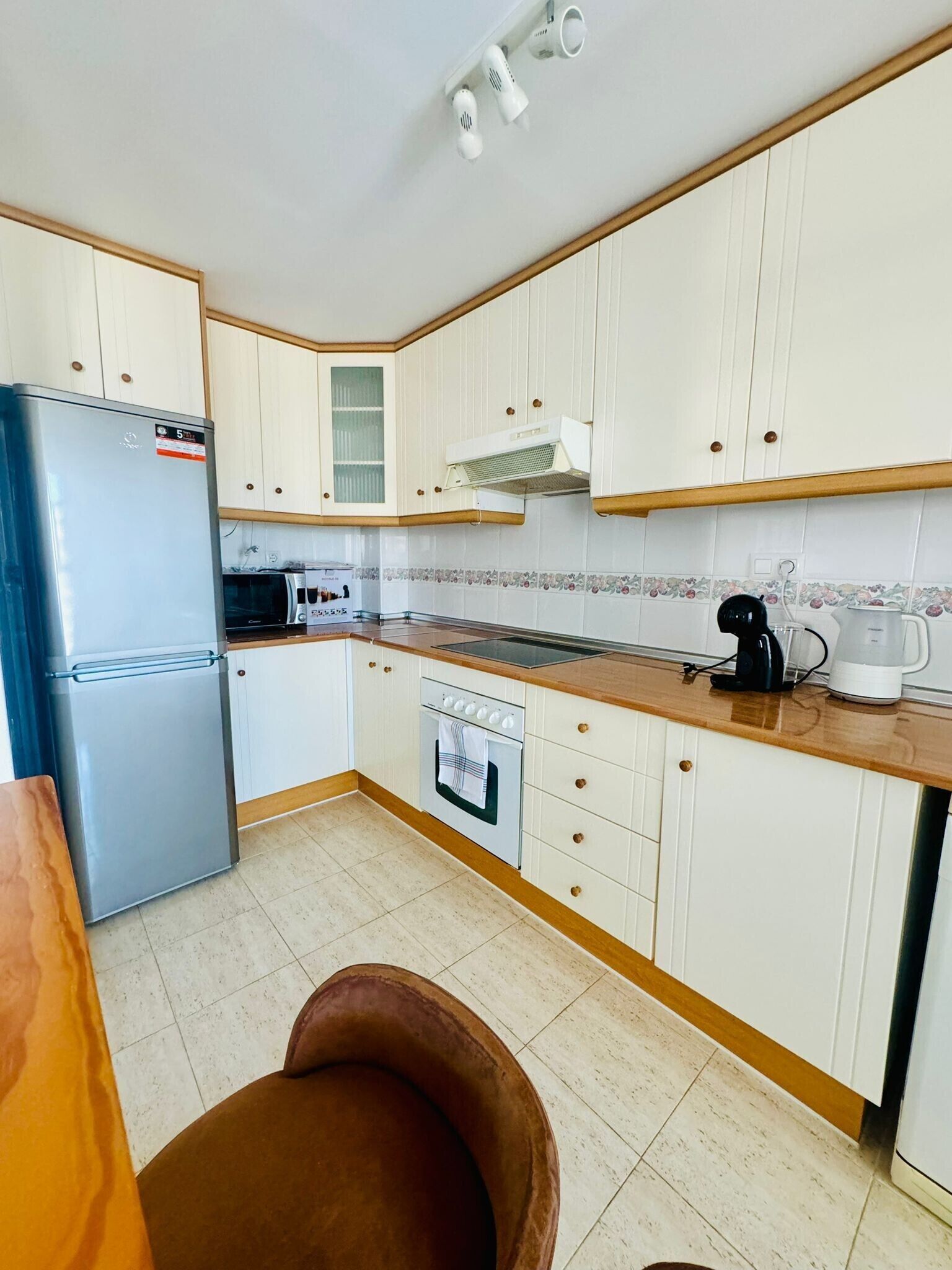 A kitchen with white cabinets, a stainless steel refrigerator, a microwave, a stove, and a coffee maker.