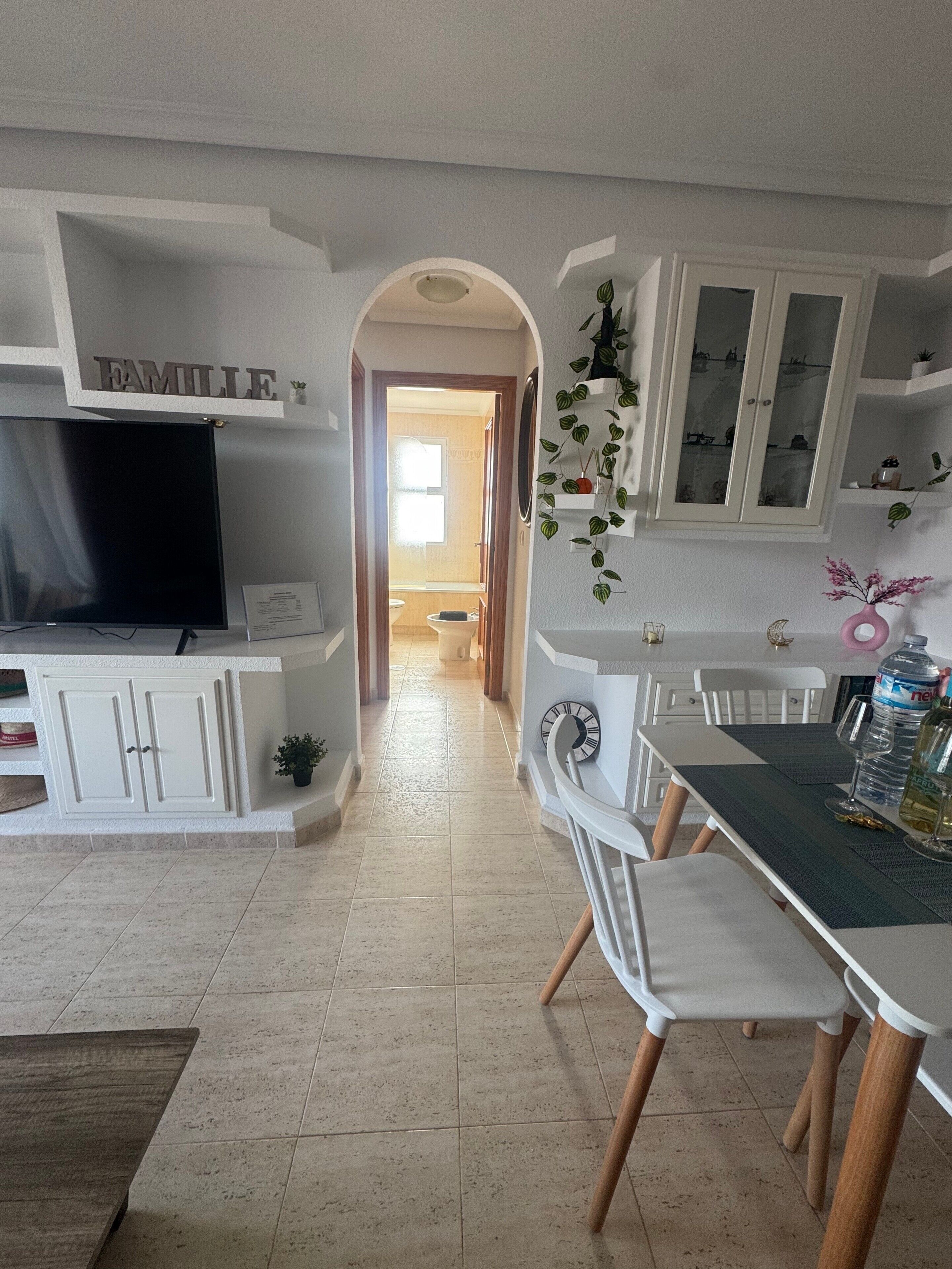 A modern kitchen with white cabinetry, a dining area with a table and chairs, and a TV mounted on the cabinetry.