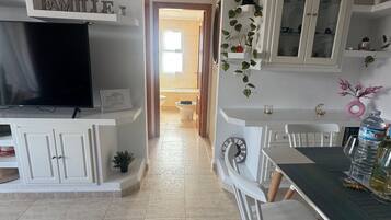 A modern kitchen with white cabinetry, a dining area with a table and chairs, and a TV mounted on the cabinetry.