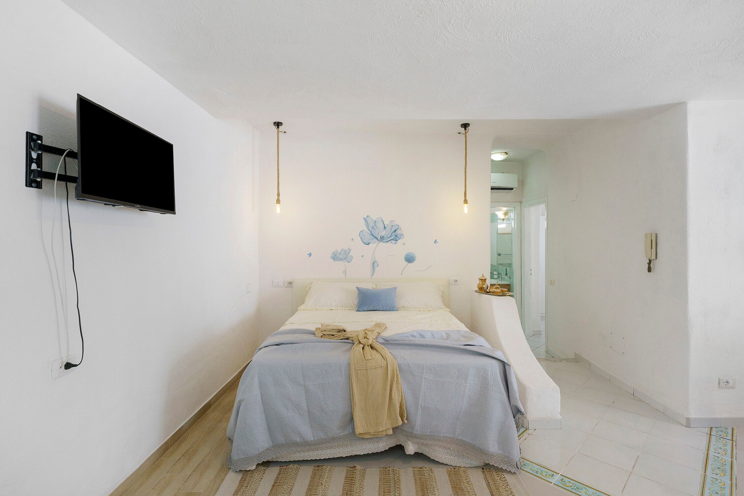 Ein Schlafzimmer mit einem Bett, einem an der Wand befestigten Fernseher und einer Wandleuchte.
