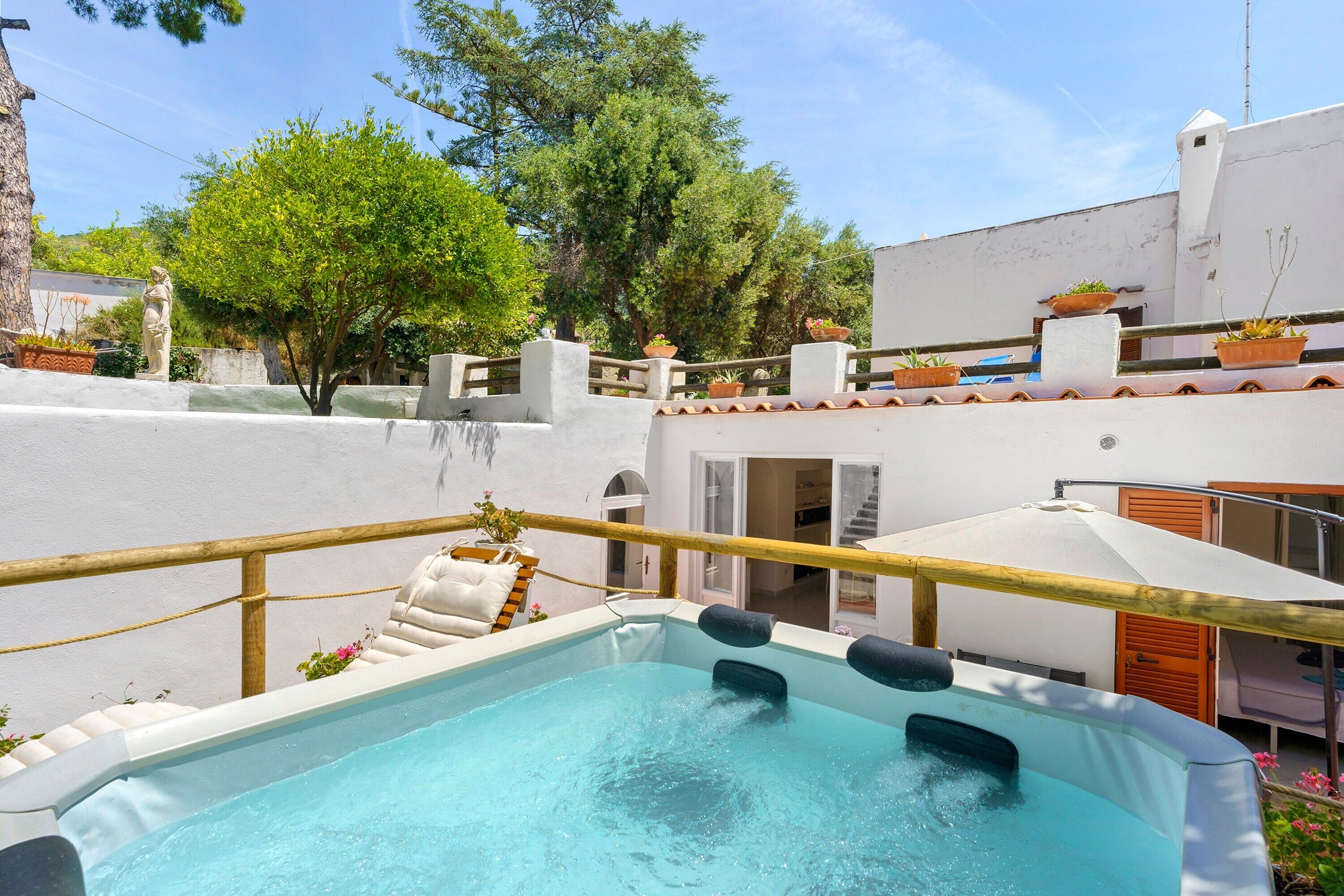 Ein Pool auf dem Dach mit Whirlpool, umgeben von Topfpflanzen und einem weißen Gebäude.