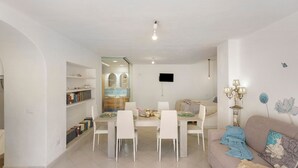 A modern living room with a dining area, a sofa, a TV mounted on the wall, and a bookshelf. - Holiday Home 'Casa Gio e Angy' with Sea View, Wi-Fi & Air Conditioning (Forio)