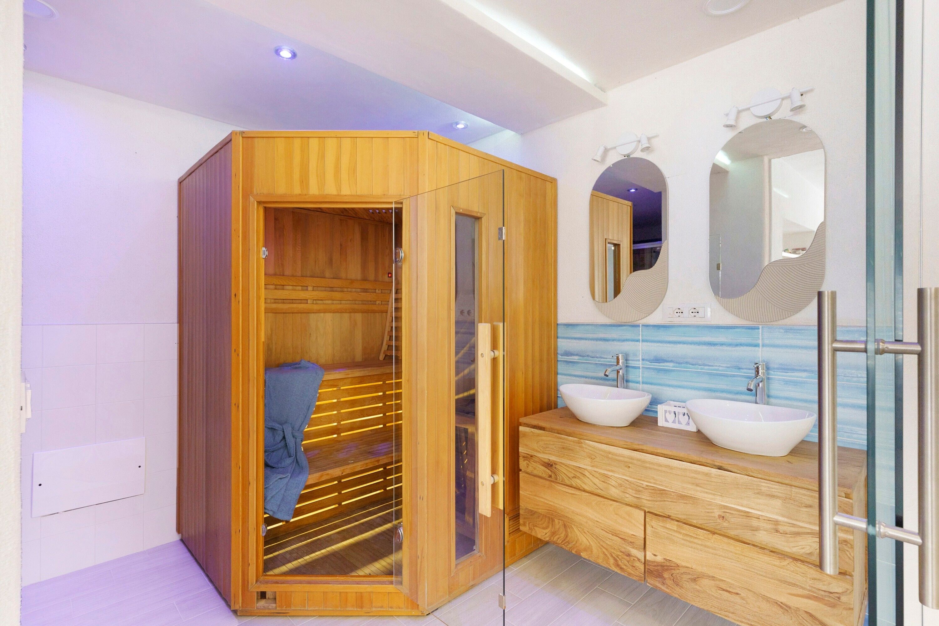 Ein modernes Badezimmer mit einer Holzauna, zwei Waschbecken und einem großen Spiegel.