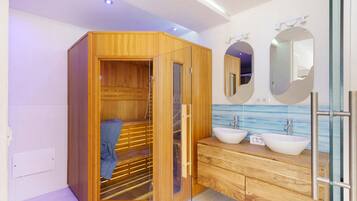 Ein modernes Badezimmer mit einer Holzauna, zwei Waschbecken und einem großen Spiegel.