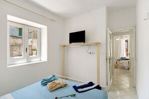 A bedroom with a bed, a television on a stand, a window, and a door leading to another room. - Holiday Home 'Casa Gio e Angy' with Sea View, Wi-Fi & Air Conditioning (Forio)