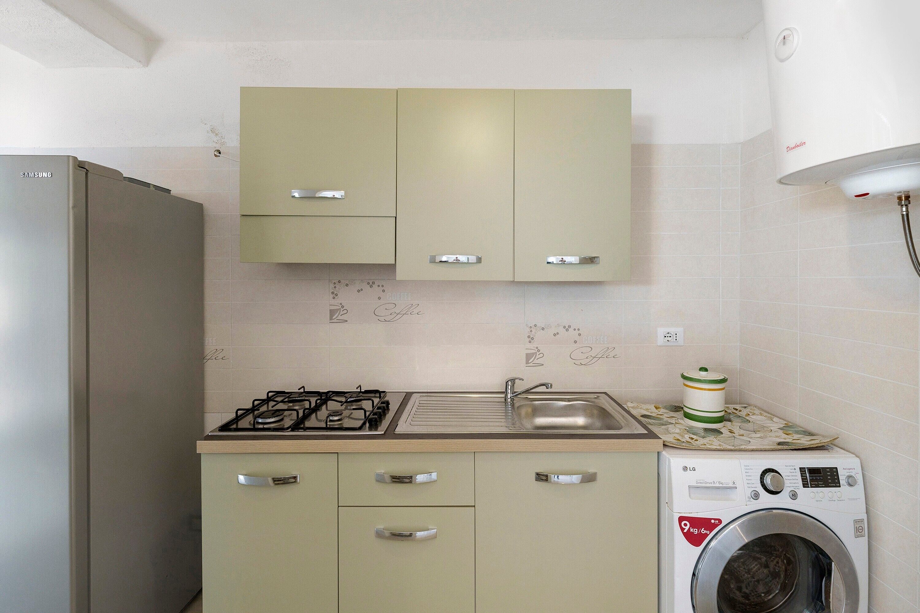 A compact kitchen with a refrigerator, gas stove, sink, and a washing machine.