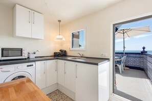 Cocina compacta con lavadora, microondas y vistas a un balcón con mesa y sillas.