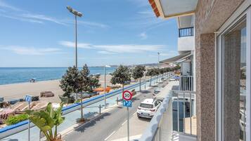 Un balcón con vista a una playa, una calle con coches estacionados y un sendero para peatones.