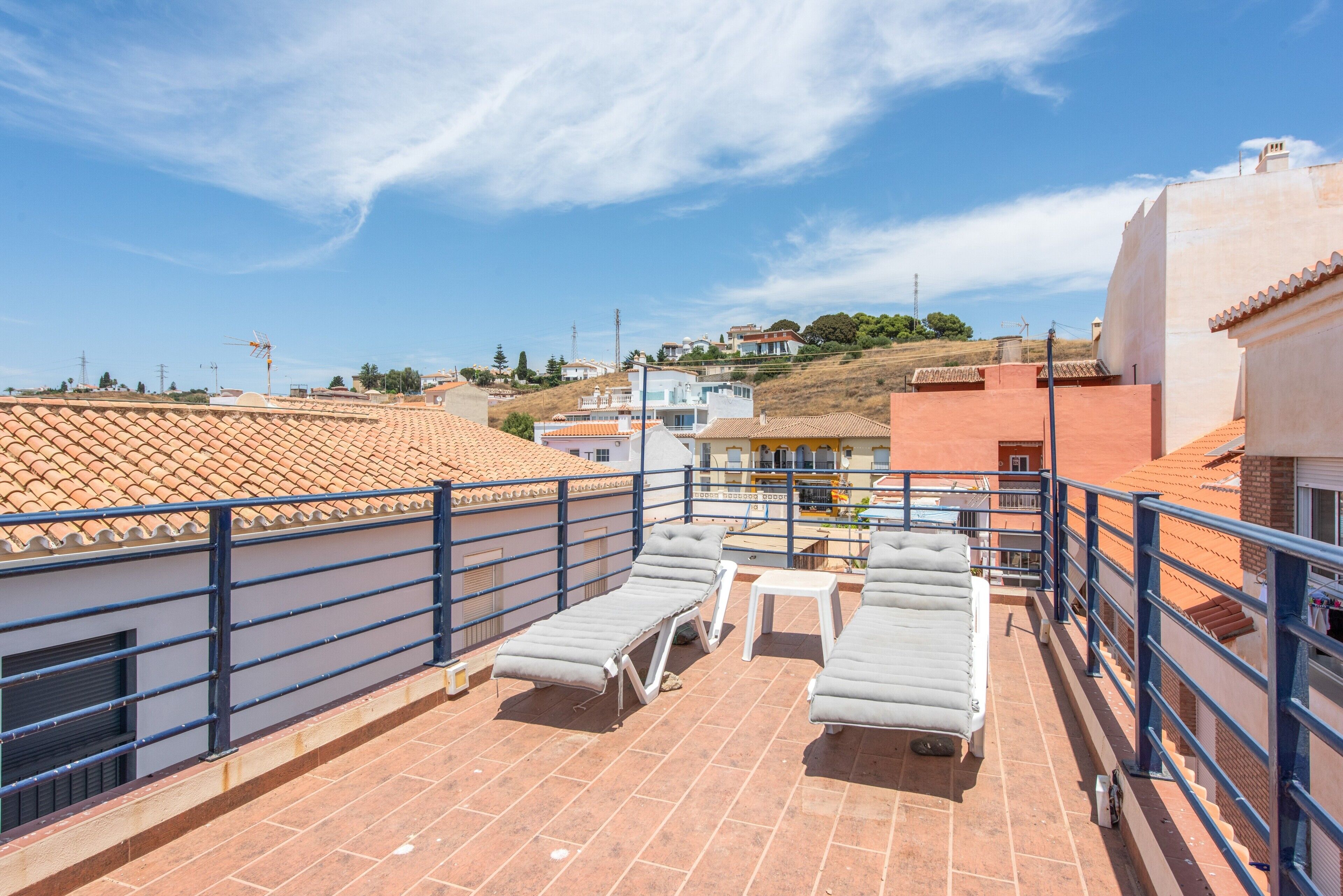 Terraza en la azotea con sillones de descanso y una mesa, con vistas a una zona residencial con tejados de teja.