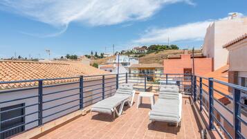 Terraza en la azotea con sillones de descanso y una mesa, con vistas a una zona residencial con tejados de teja.