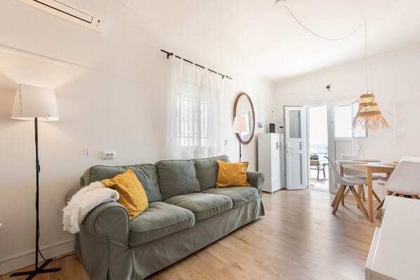 A living room with a sofa, a lamp, a dining table, and a view through an open door.