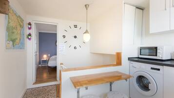 Una cocina compacta con lavadora, microondas, una mesa de madera y un reloj de pared.