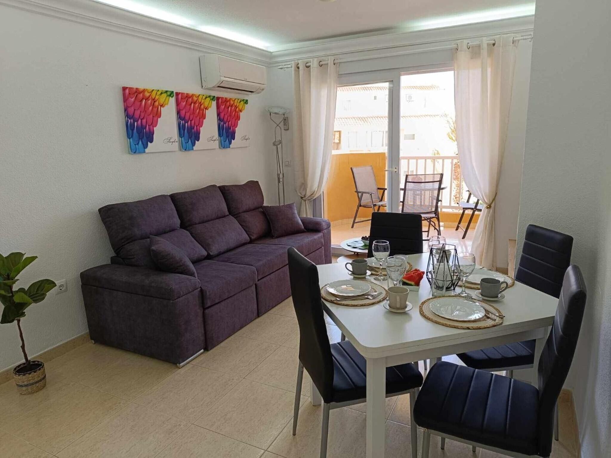 Un salon avec un canapé, une table à manger dressée pour deux personnes et un balcon avec des chaises.