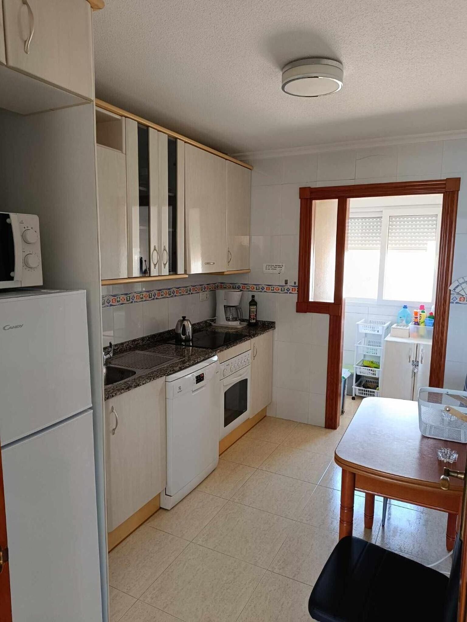 Una cocina compacta con armarios blancos, microondas, cafetera y lavabo.