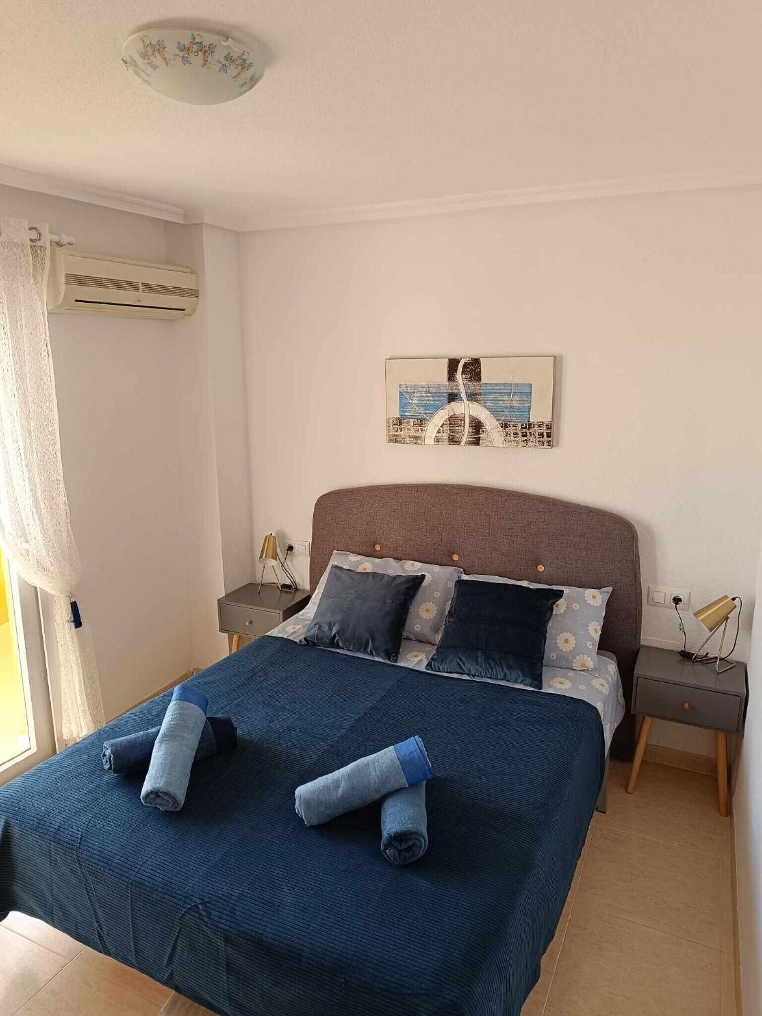 A bedroom with a bed, a nightstand, a lamp, and a wall-mounted picture.