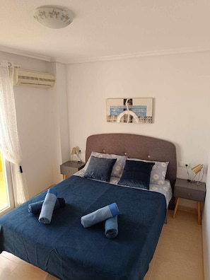 Ein Schlafzimmer mit Bett, Nachttisch, Lampe und einem an der Wand hängenden Bild.