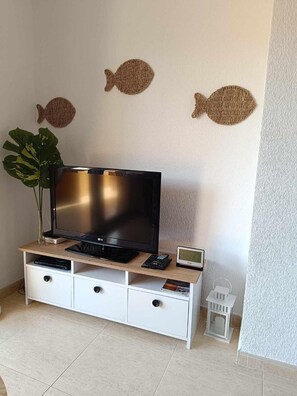 Ein Flachbildfernseher auf einem Holz-TV-Schrank mit Fernbedienung und einer Uhr, eine Pflanze und drei an der Wand befestigte Fischdekorationen.