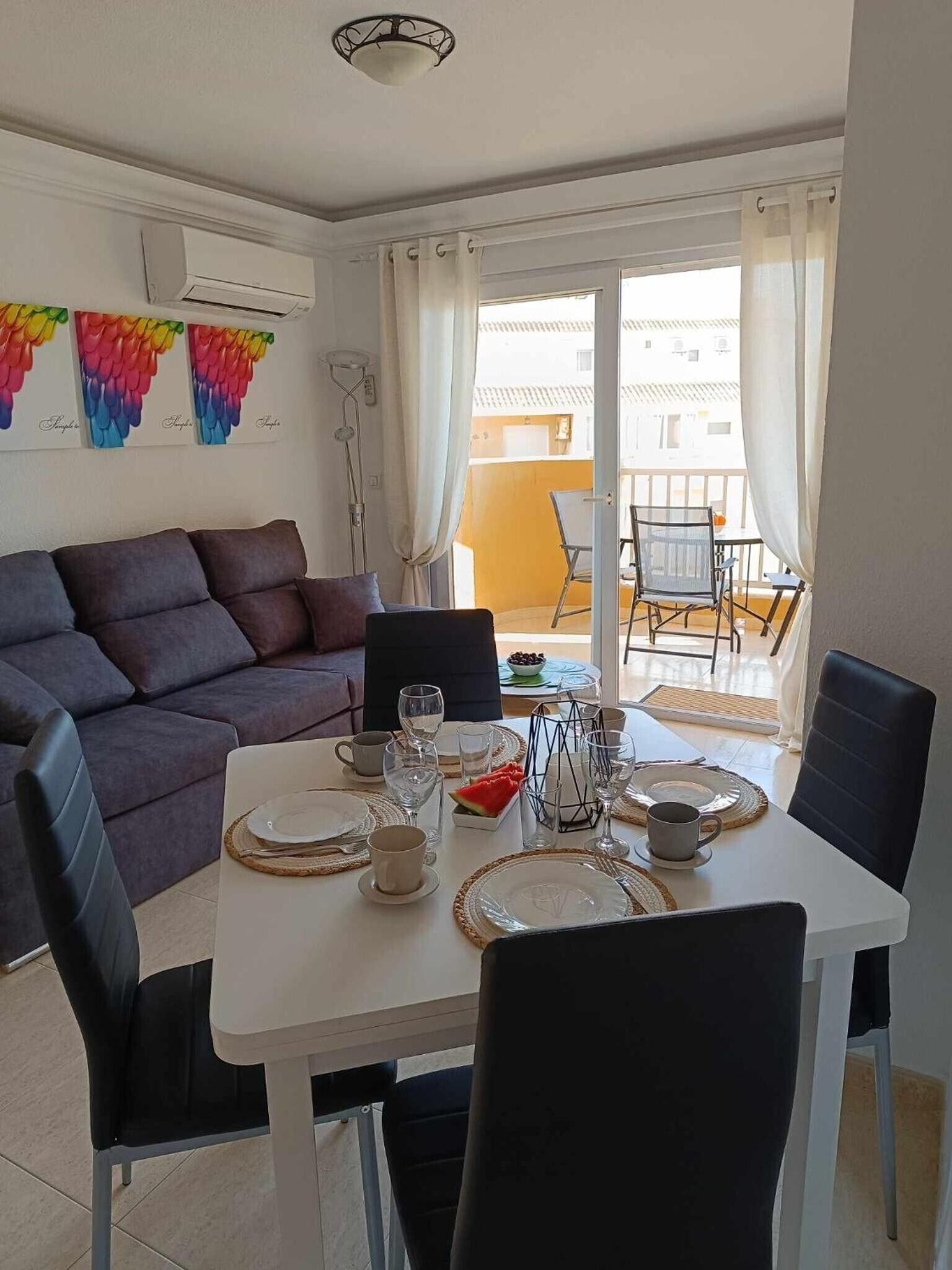 A dining area with a white table set for four, surrounded by black chairs.