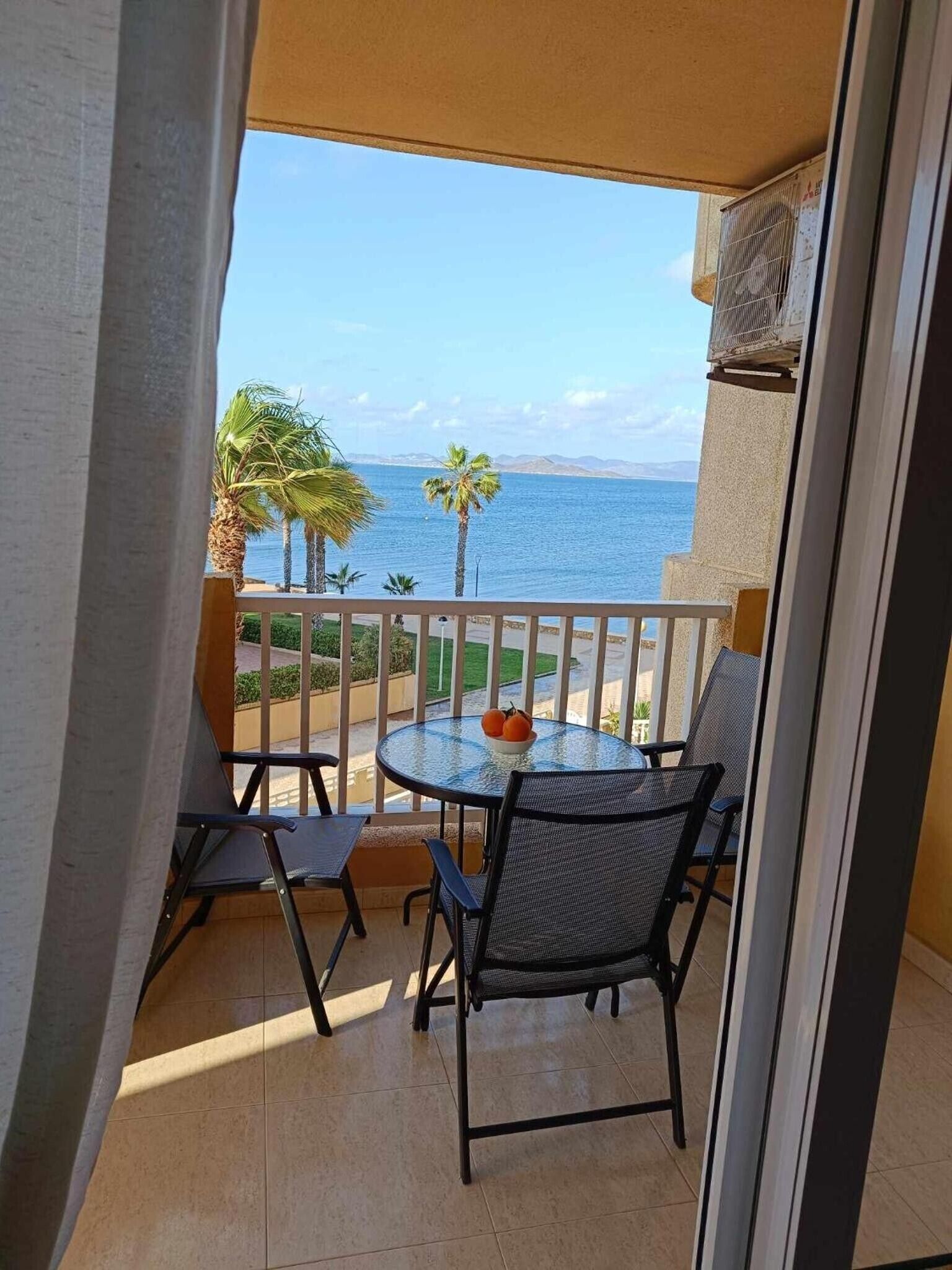 A balcony with a table and chairs, overlooking a body of water and palm trees.