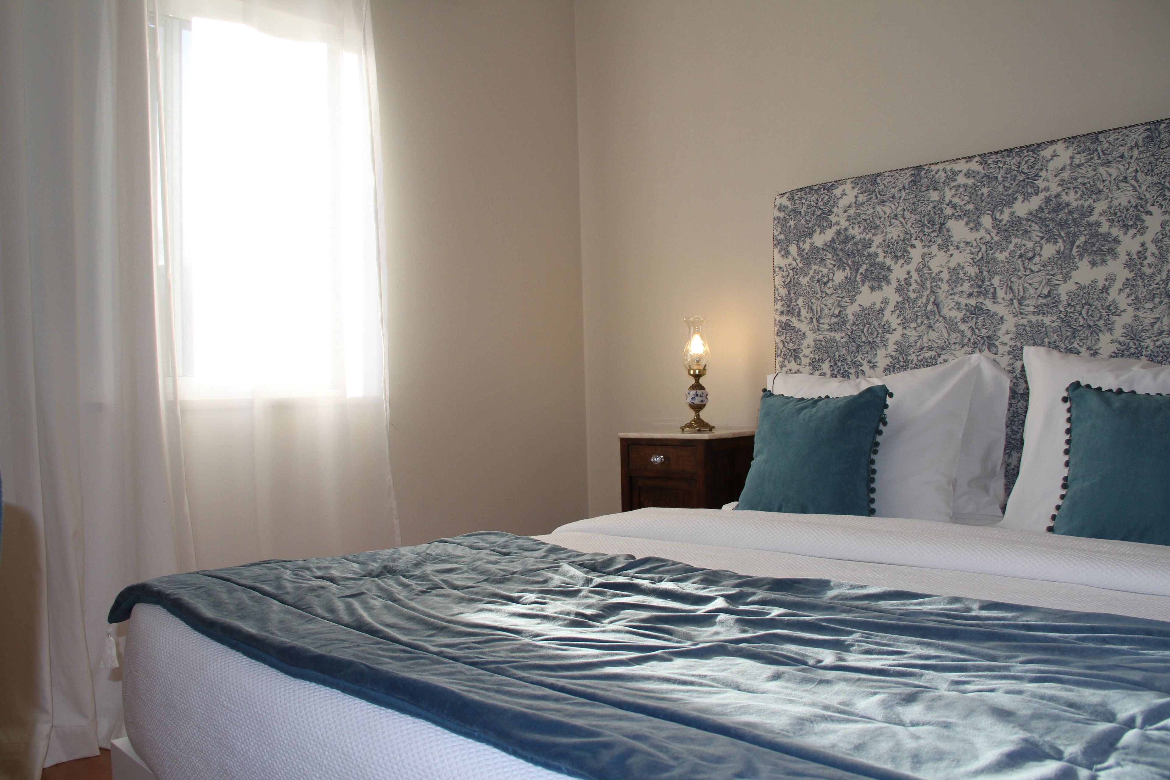 A bedroom with a bed, a nightstand, a lamp, and a window with curtains.