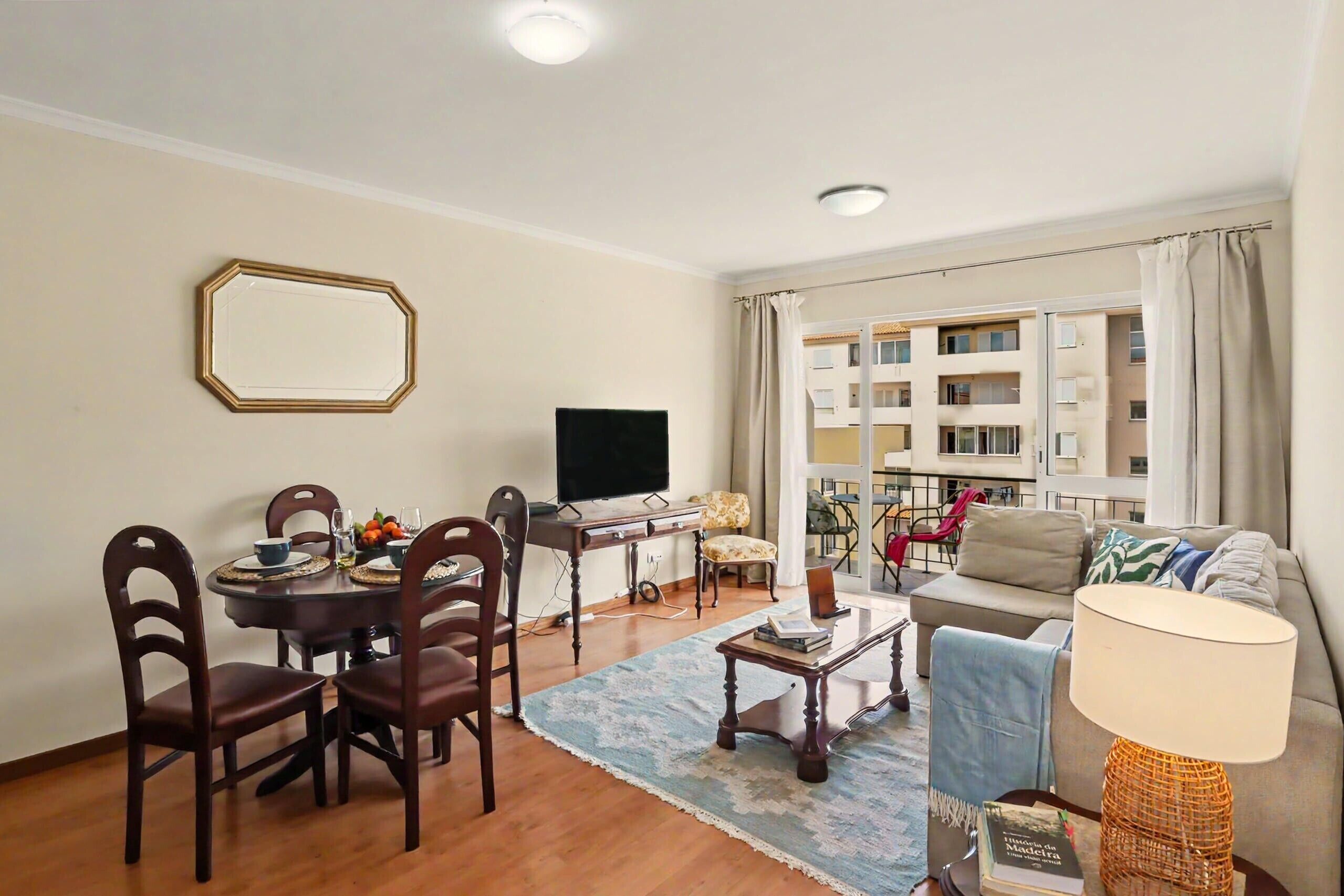 A living room with a dining table, chairs, a TV, a sofa, and a window with curtains.